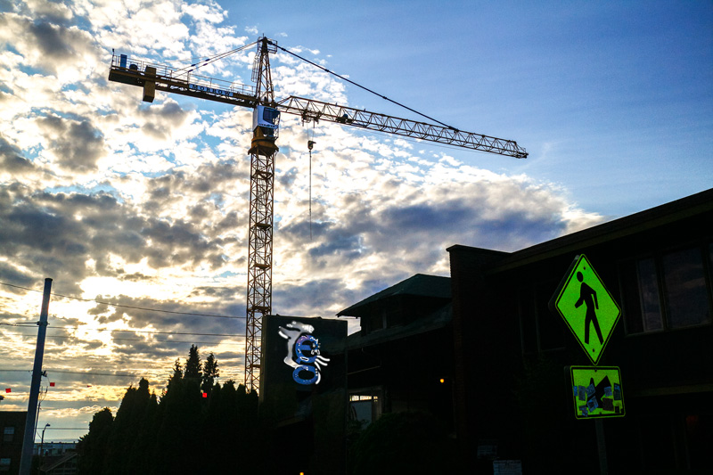 Photo of a construction crane in the distance, with strange creatures on a street sign in the foreground