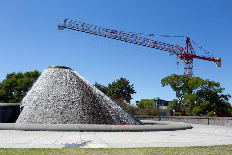 Photo of a large construction crane looming above a scultptural fountain